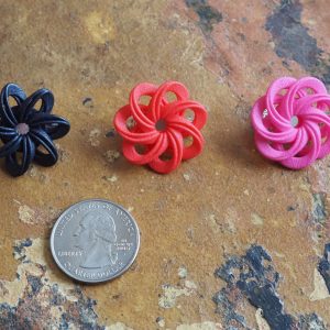 Three flower-like nylon pins, black, red, and pink, on a glazed tile surface with a US quarter for size.